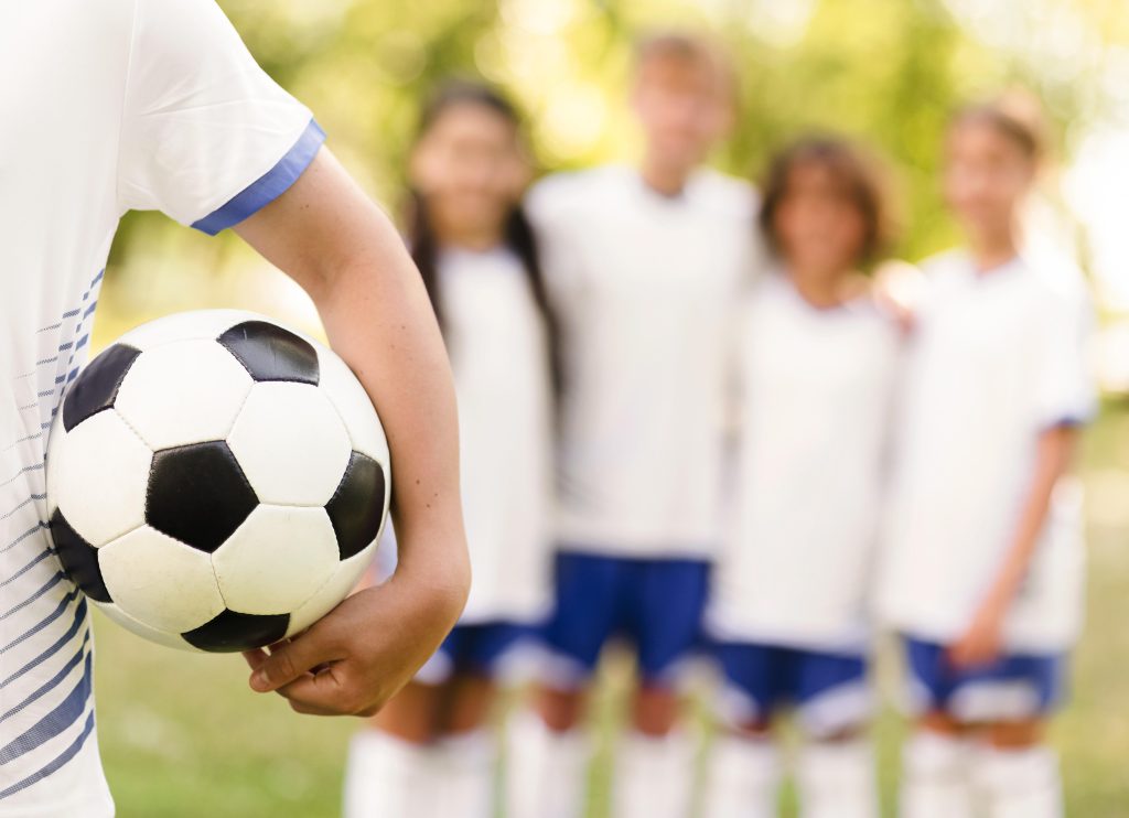 boy-holding-football-his-team-mates-unfocused
