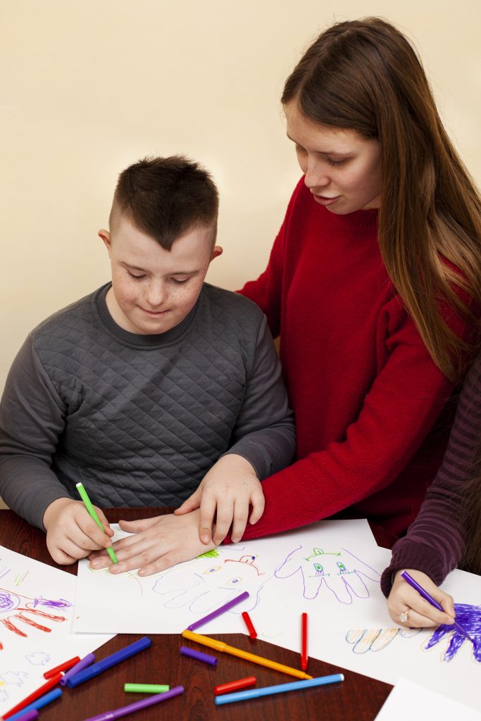 woman-helping-boy-with-down-syndrome-draw